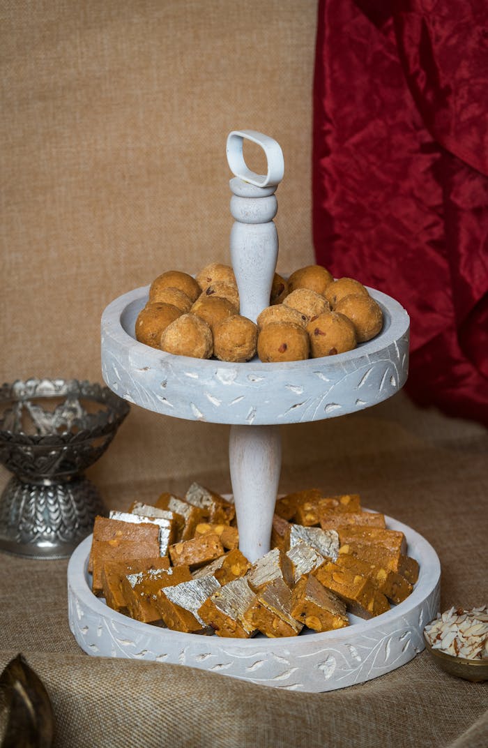 A beautiful display of traditional Indian sweets on a rustic two-tier tray with a vibrant backdrop.