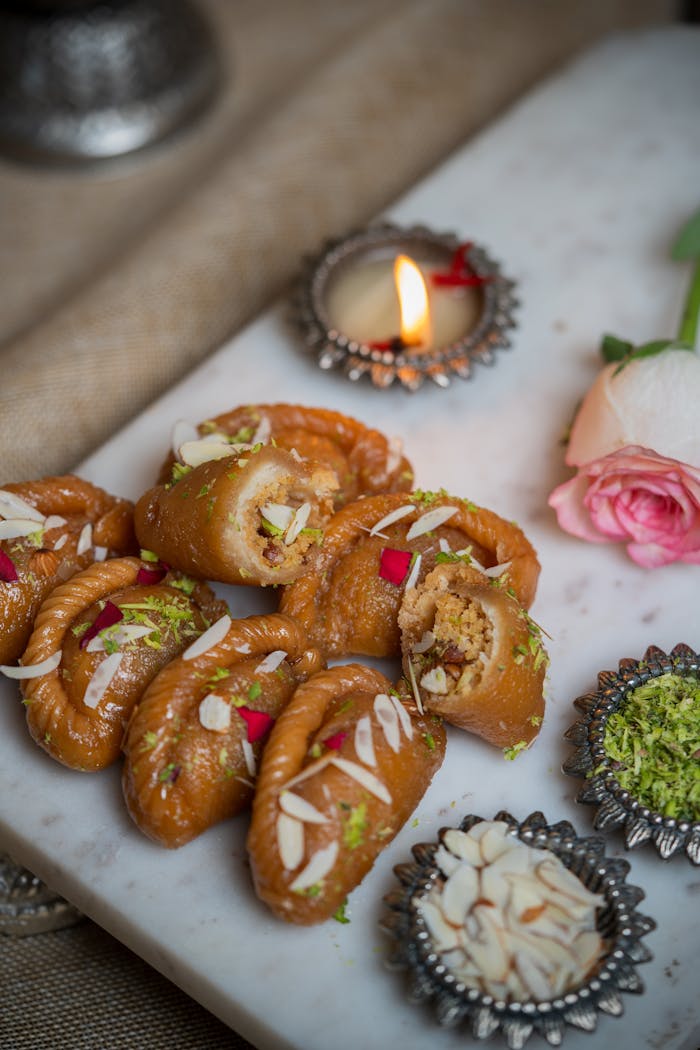 Close-up of Indian sweets with a lit diya and rose on a marble tray.