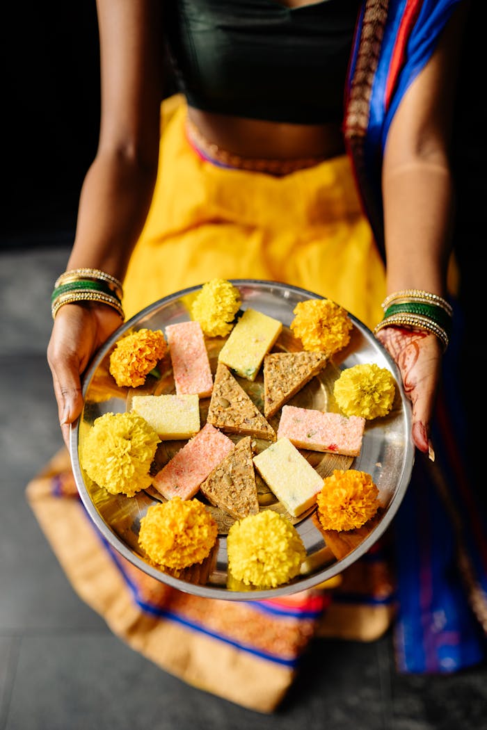 A woman holds a platter of vibrant Indian sweets and marigold flowers, celebrating Diwali.